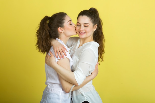 Dos hermosas mujeres gemelas alegres sobre un fondo amarillo