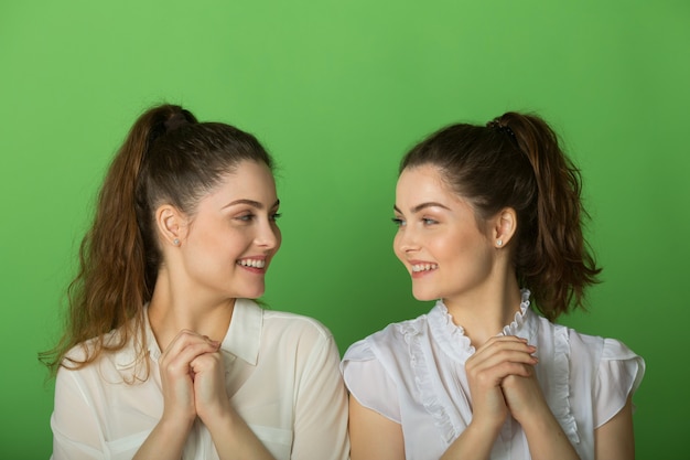 Dos hermosas mujeres gemelas alegres sobre un fondo verde