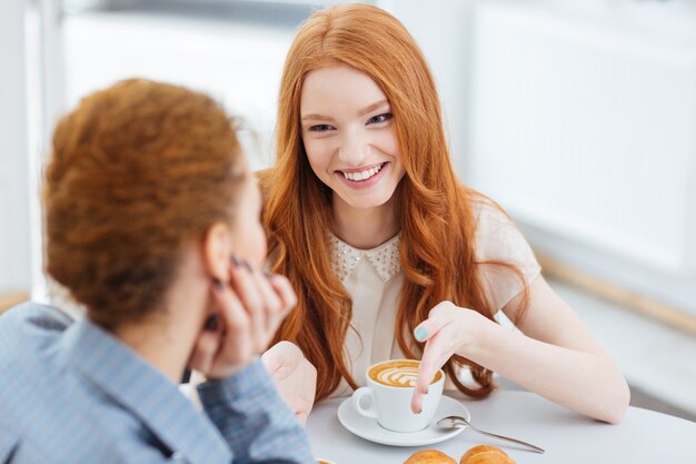 Dos hermosas mujeres jóvenes alegres sentados juntos en la cafetería