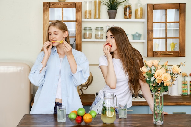 Dos hermosas mujeres jóvenes comen frutas en la cocina