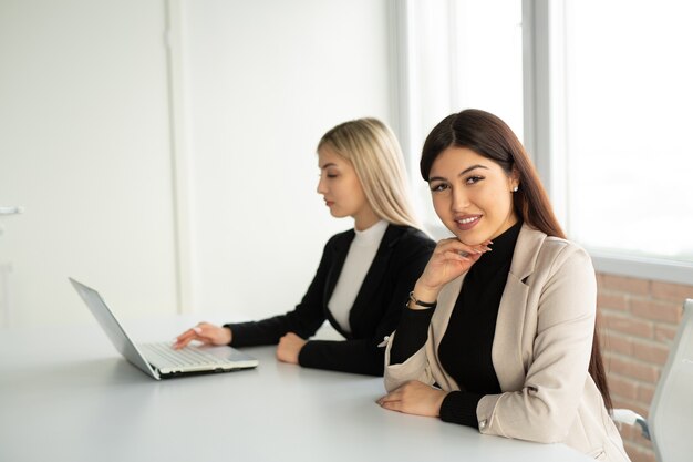 Dos hermosas mujeres jóvenes en la mesa de la oficina con una computadora portátil