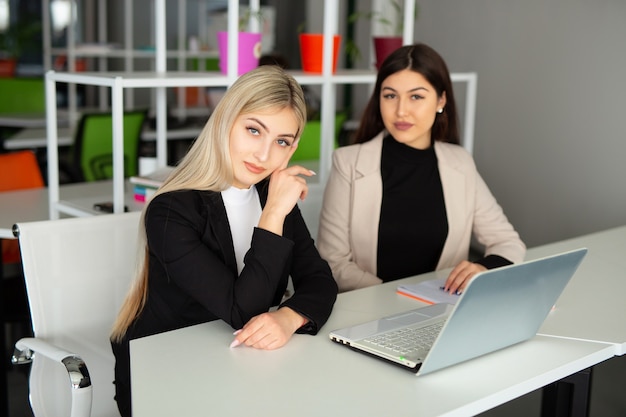 dos hermosas mujeres jóvenes en la oficina con una computadora portátil