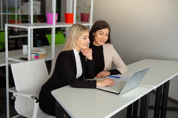 dos hermosas mujeres jóvenes en la oficina con una computadora portátil