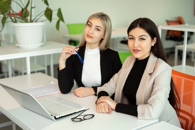 Dos hermosas mujeres jóvenes en la oficina en la mesa con una computadora portátil