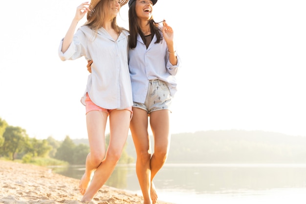 Dos hermosas mujeres jóvenes paseando por una playa. Amigas caminando por la playa y riendo en un día de verano.