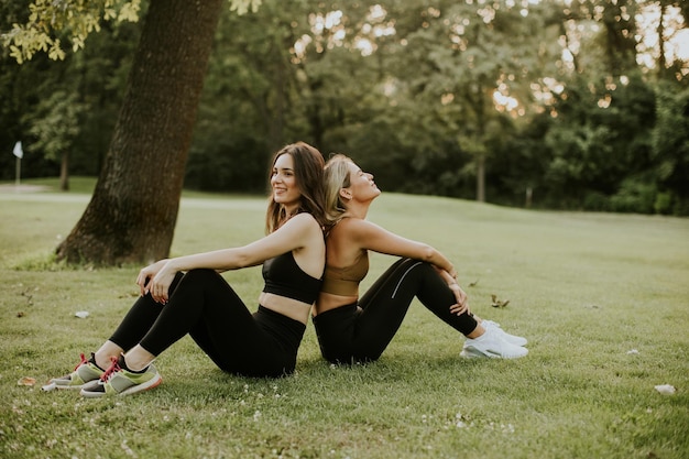 Dos hermosas mujeres jóvenes sentadas en el césped y relajándose después de un entrenamiento al aire libre