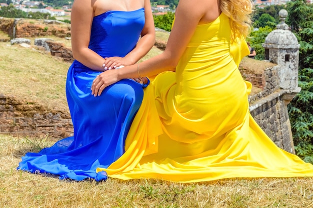 Dos hermosas mujeres jóvenes en vestidos azules y amarillos cogidos de la mano de rodillas, concepto amor lésbico