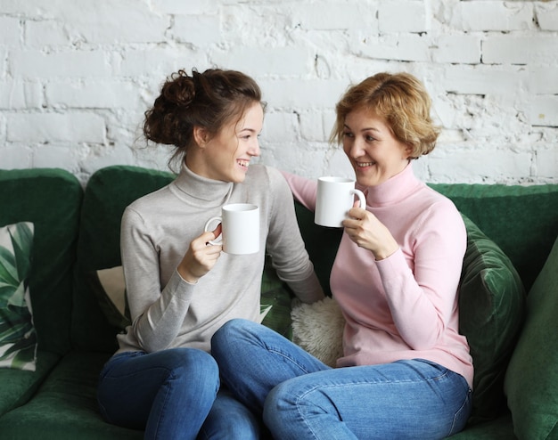 Dos hermosas mujeres madre e hija sentadas en el sofá de casa y tomando café o té