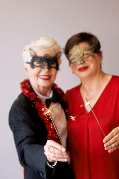 Dos hermosas mujeres mayores maduras con estilo en máscaras de carnaval con destellos celebrando el año nuevo