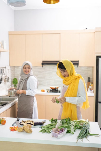 Dos hermosas mujeres musulmanas disfrutan cocinando la cena juntos para iftar rompiendo el ayuno en ramadán en la cocina