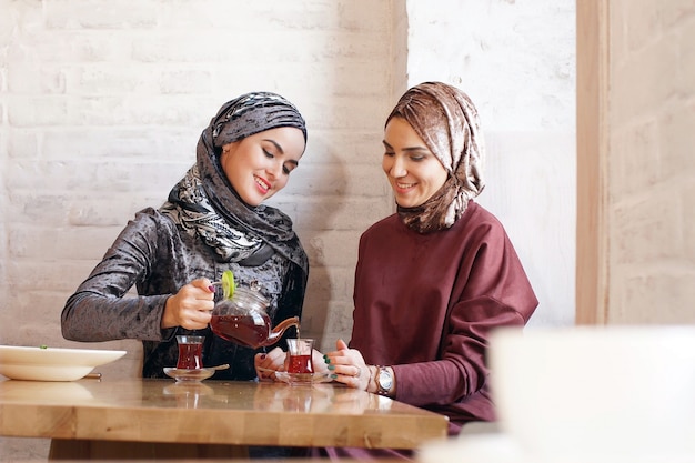 Dos hermosas mujeres musulmanas en hijabs beben té en la cafetería