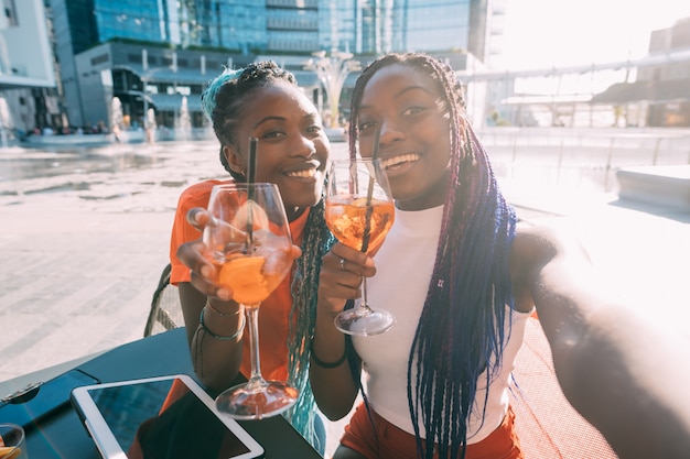 Dos hermosas mujeres negras hermanas sentado bar haciendo un brindis sonriendo