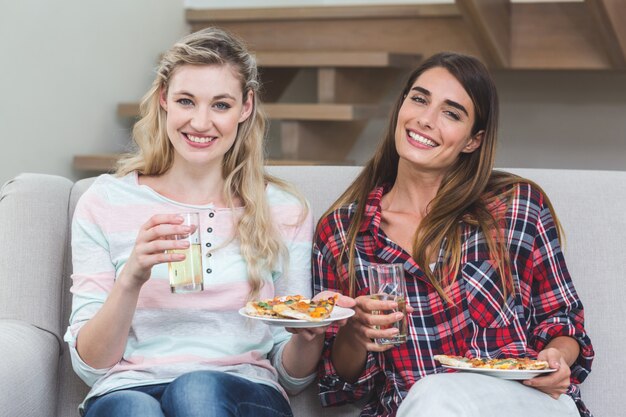 Dos hermosas mujeres sentadas en el sofá y comiendo pizza