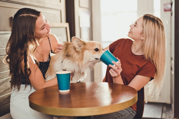 Dos hermosas mujeres tomando café con un perro corgi