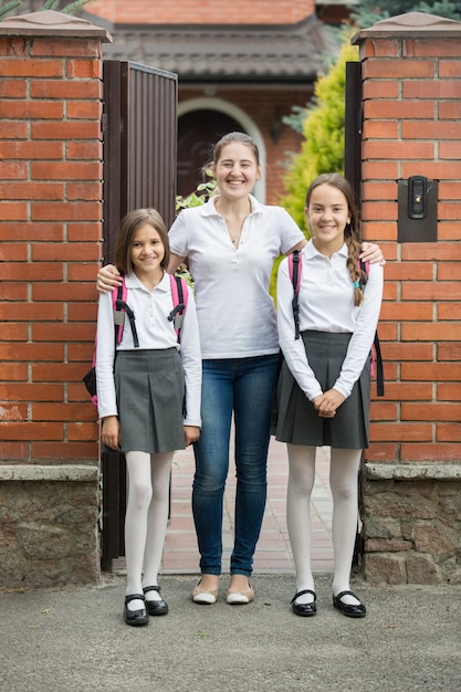 Dos hermosas niñas de pie con su madre en la puerta antes de ir a la escuela