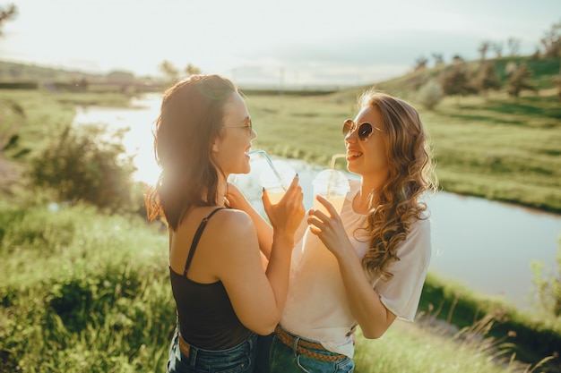 Dos hermosas novias chicas beben cócteles divirtiéndose verano, al atardecer, expresión facial positiva, al aire libre