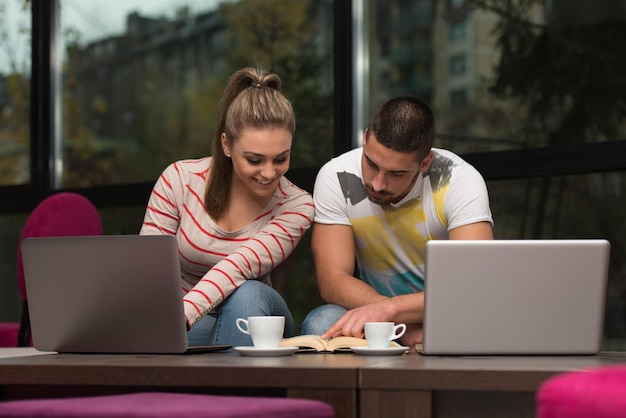 Dos hermosos estudiantes bebiendo y divirtiéndose con la computadora portátil en la cafetería