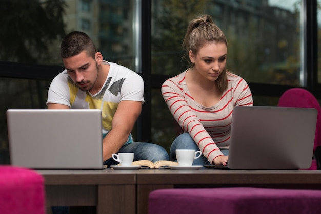 Dos hermosos estudiantes bebiendo y divirtiéndose con la computadora portátil en la cafetería