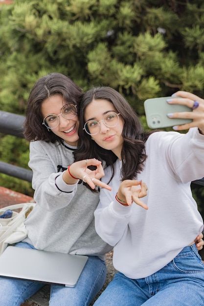 Foto dos hermosos gemelos sonriendo y tomándose un selfie en un parque.