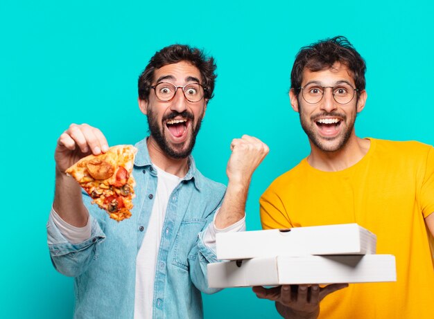 Dos hispanos pareja de amigos celebrando una victoria exitosa y sosteniendo pizzas para llevar