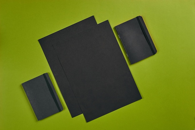 Dos hojas de papel negro y carpetas sobre fondo verde con espacio de copia Concepto de lugar de trabajo educativo Vista superior enfocada con diferentes suministros de equipo de oficina Papelería Primer plano