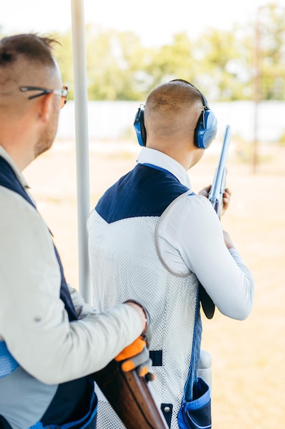 Dos hombres adultos con gafas de sol y un chaleco de rifle practicando tiro con armas de fuego