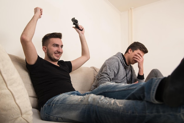 Dos hombres amigos competitivos jugando videojuegos y emocionados felices alegres en casa