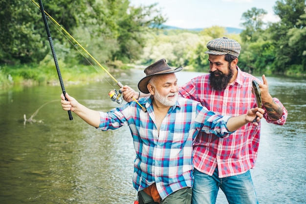 Dos hombres amigos pesca Flyfishing pescador hace yeso de pie en el agua del río viejo y joven pescador feliz emocionado hombre amigos