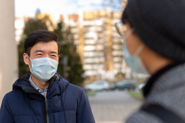 Dos hombres asiáticos con máscaras médicas contra covid-2019 sonríen y hablan entre sí