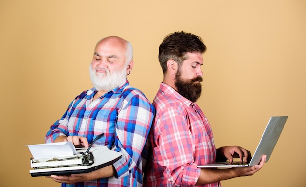 Dos hombres barbudos Batalla de generación de tecnología de máquina de escribir vintage Vida moderna desarrollo y mejora de tecnología de padre e hijo máquina de escribir retro vs portátil juventud vs vejez enfoque empresarial