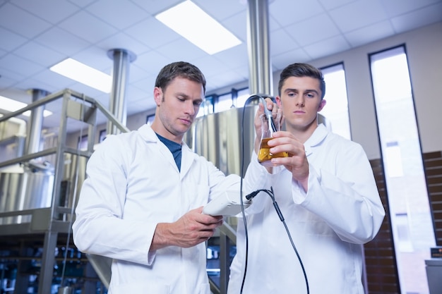 Dos hombres en bata de laboratorio probando cerveza en el vaso de precipitados