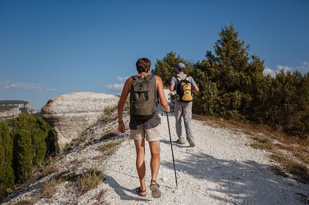 Dos hombres caminando sobre una ladera rocosa llevando mochilas usando bastones de trekking