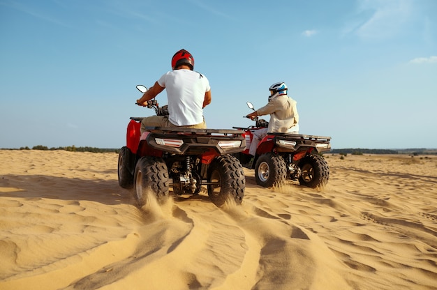 Dos hombres con cascos montados en atv en las arenas del desierto