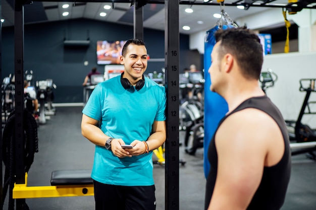 Foto dos hombres entrenando en el gimnasio mirando el teléfono móvil