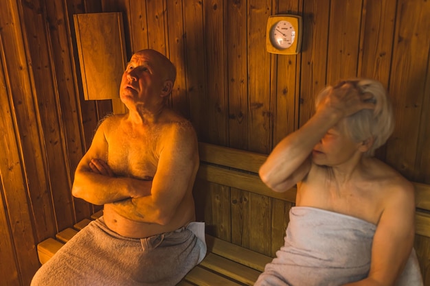 Dos hombres están sentados en una sauna, uno de ellos lleva una toalla.