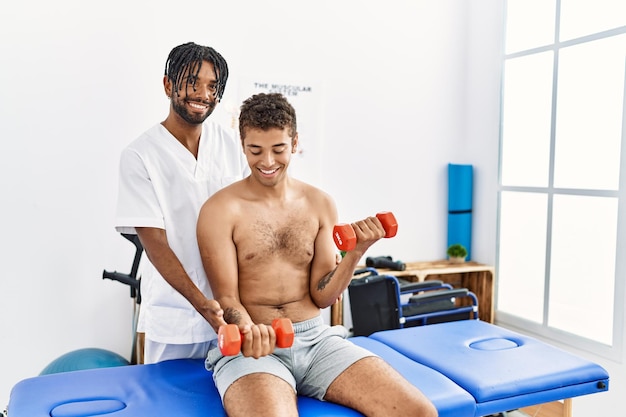 Foto dos hombres fisioterapeuta y paciente en sesión de rehabilitación usando pesas en la clínica