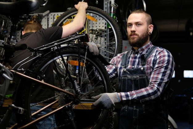 Dos hombres guapos y elegantes que trabajan con una bicicleta en un taller de reparación. Los trabajadores reparan y montan bicicletas en un taller.