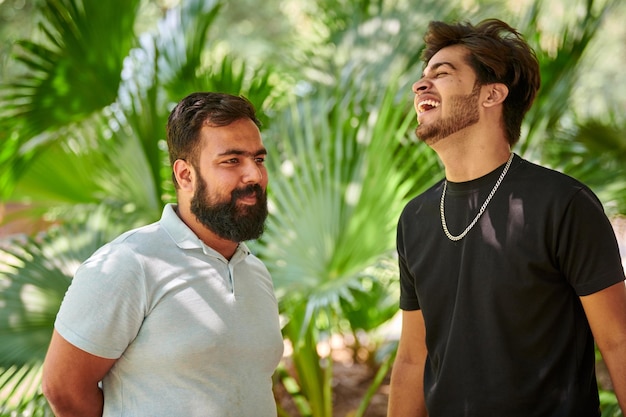 Dos hombres indios divertidos riendo y hablando hindi en un parque público fondo de hojas de palma verde