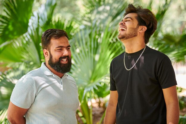 Dos hombres indios divertidos riendo y hablando hindi en un parque público fondo de hojas de palma verde