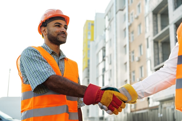 Dos hombres ingenieros en ropa de trabajo un apretón de manos contra el sitio en construcción