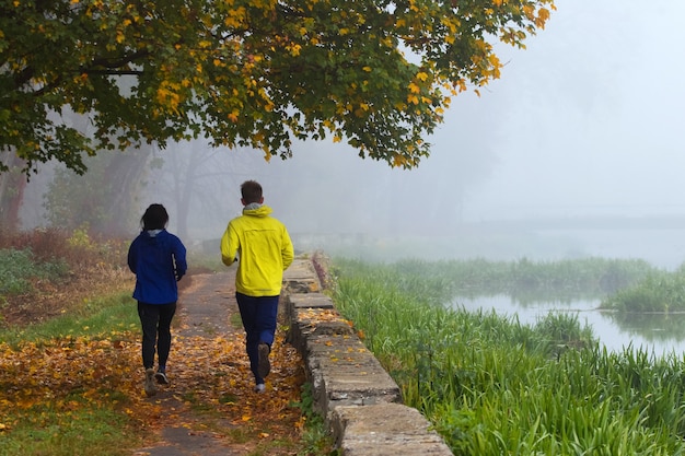 Dos hombres jóvenes, un chico y una chica, corren por la mañana en el parque de otoño