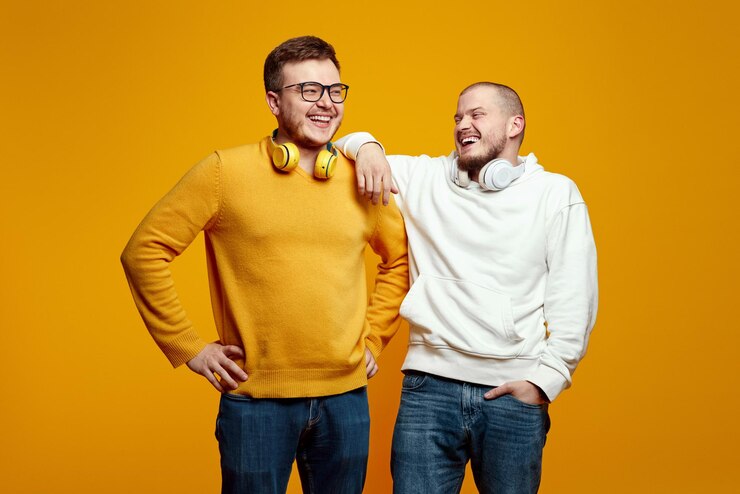 Dos hombres jóvenes y guapos amigos con auriculares con trajes casuales riendo y divirtiéndose en