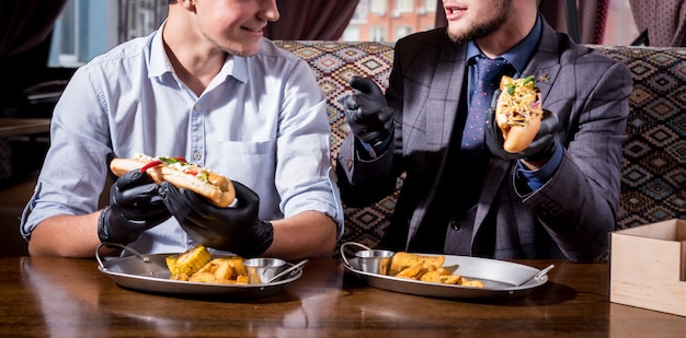 Dos hombres jóvenes hambrientos comiendo hot dogs en café. restaurante