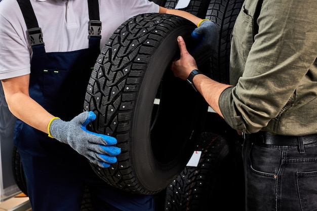 Dos hombres mirando la superficie del neumático de automóvil discutiendo las ventajas de los neumáticos de invierno para automóviles, conversan, tocan y examinan