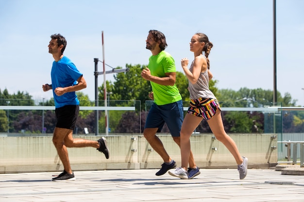 Foto dos hombres y una mujer jóvenes corriendo en un entorno urbano.