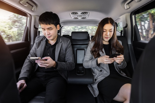 Foto dos hombres y mujeres de negocios con smartphone mientras están sentados en el asiento trasero de un coche