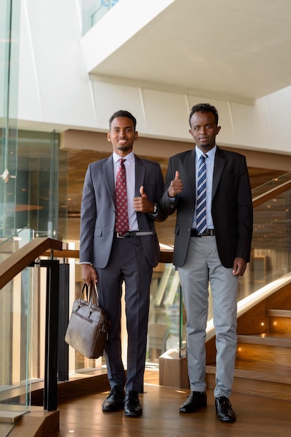 Dos hombres de negocios africanos con traje y corbata en la cafetería.