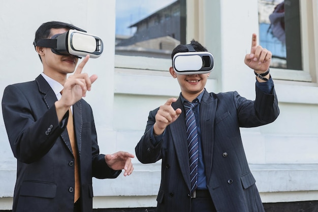 Dos hombres de negocios asiáticos con traje formal usan gafas VR fuera de la oficina Estilo de vida de entretenimiento a