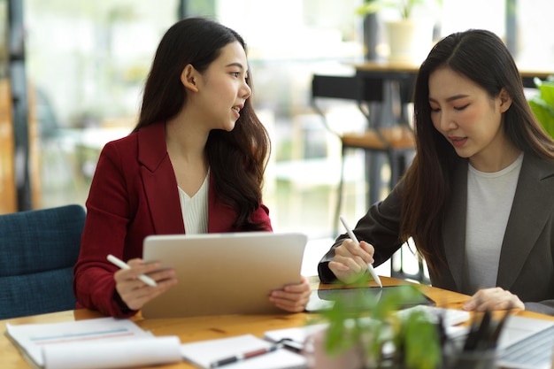 Dos hombres de negocios atractivos que usan una tableta digital juntos mientras trabajan, discuten y analizan los datos en el escritorio en una oficina moderna