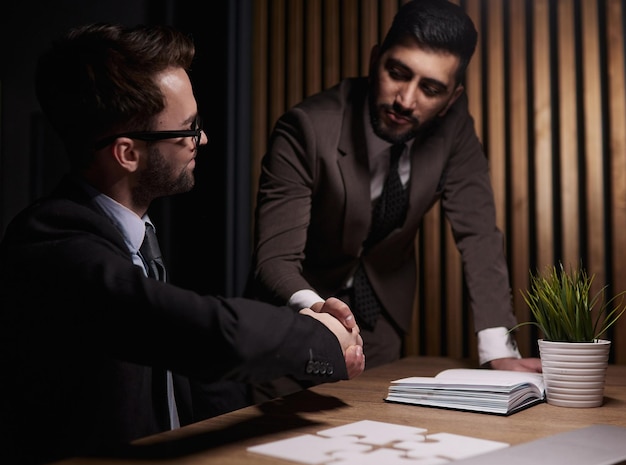 Dos hombres de negocios confiados dándose la mano en la mesa de la oficina